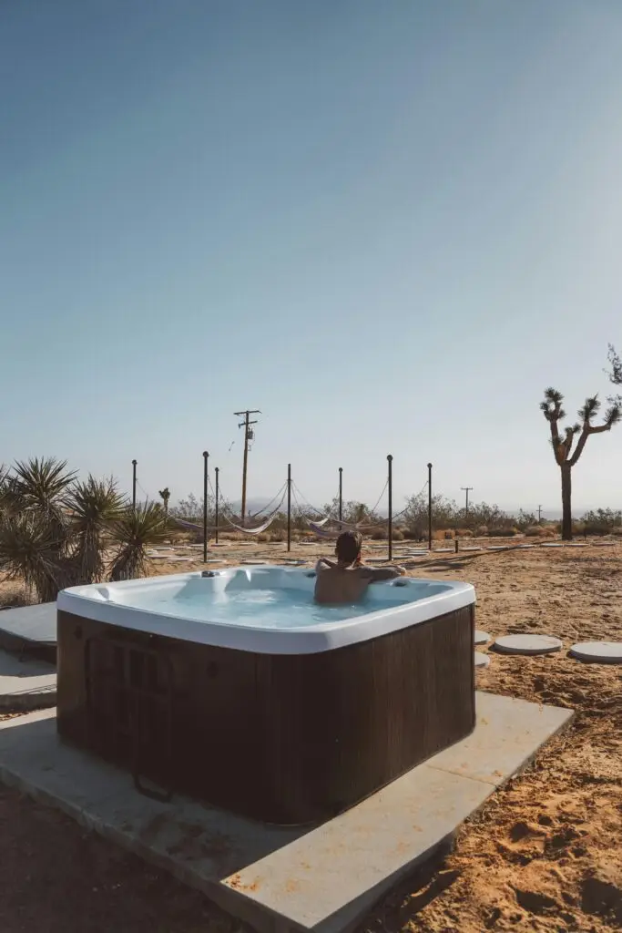 Man enjoying a hot tub in the serene landscape of Joshua Tree desert under a clear blue sky.
